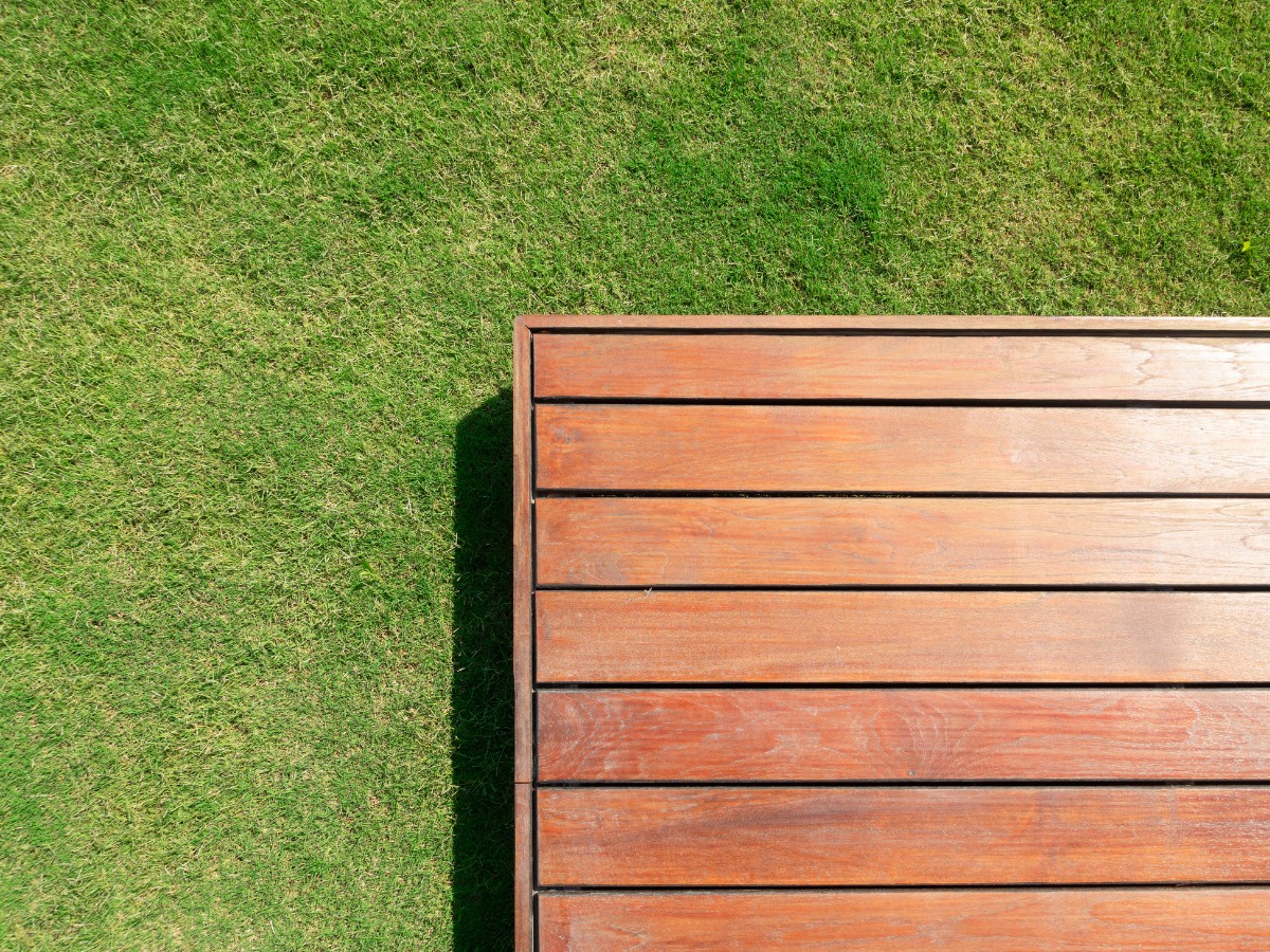 A nicely varnished decking set over a patch of grass, representing gardens and patios